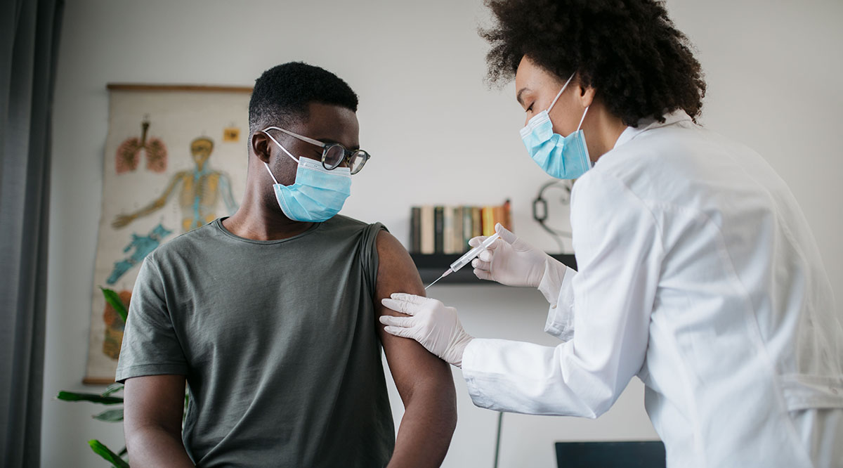 Black physician give Black patient vaccine.