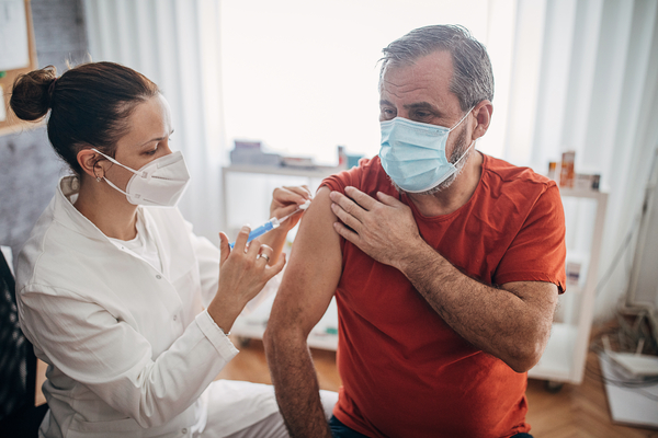 Young female doctor injecting vaccine in arm of senior man for immunization.