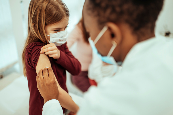 Masked adolescent patient receives vaccination from masked physician. 