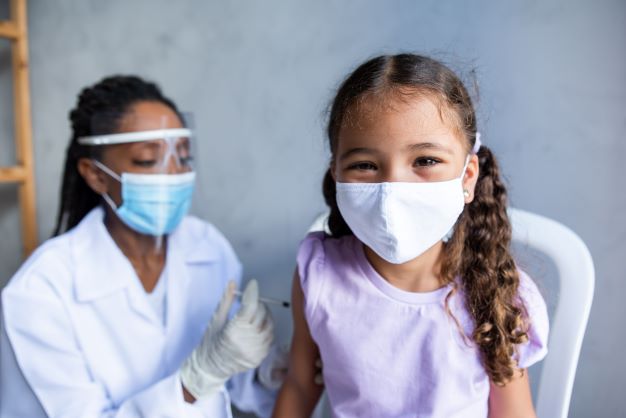 A masked nurse administers a vaccination to a masked adolescent patient. 