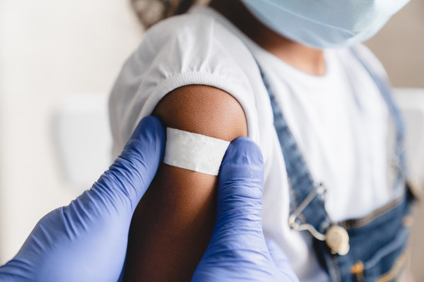 A gloved medical work places a band-aid on a masked child patient. 