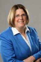 Janet Englund poses in a blue blazer and a white-collared top with her arms crossed. 