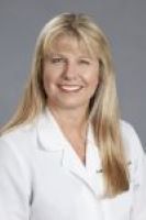 Lisa Gwynn smiles in her white coat on a gray backdrop. 