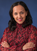 Jameela Yuseff poses in a long sleeve red top with her arms crossed on a navy backdrop.