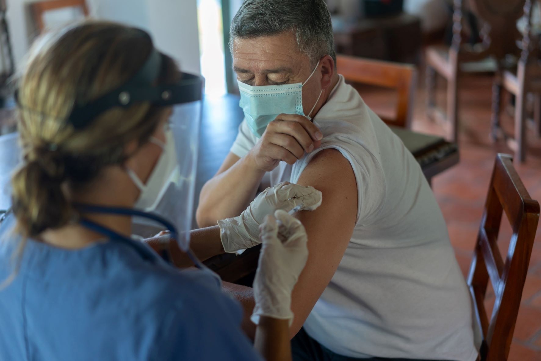 A nurse administers a vaccination to a masked patient. 