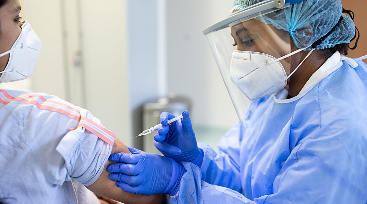 Nurse applying vaccine on patient's arm. Both are wearing face masks.