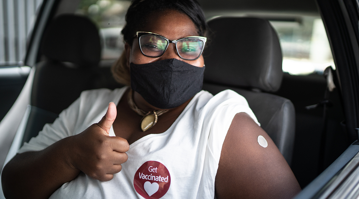 Portrait of a happy woman in a car with a 'get vaccinated' sticker - wearing face mask