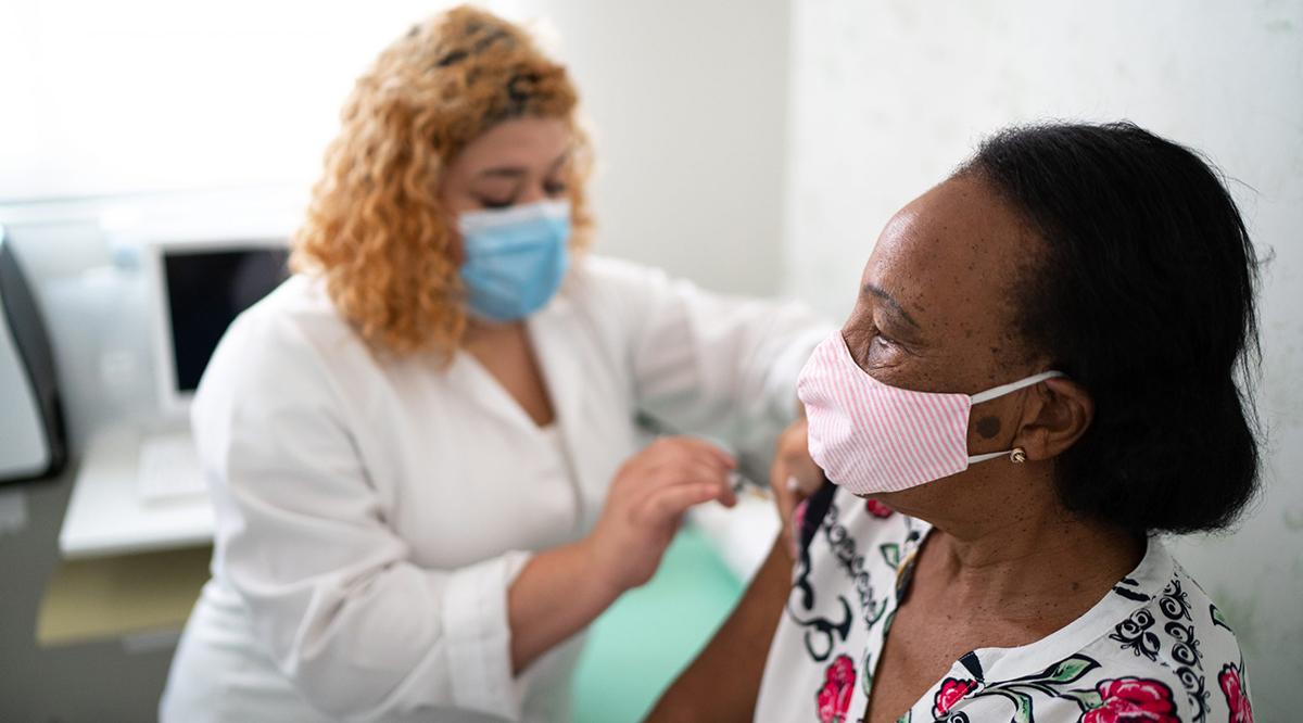 Nurse applying vaccine on patient's arm. Both are wearing face masks.