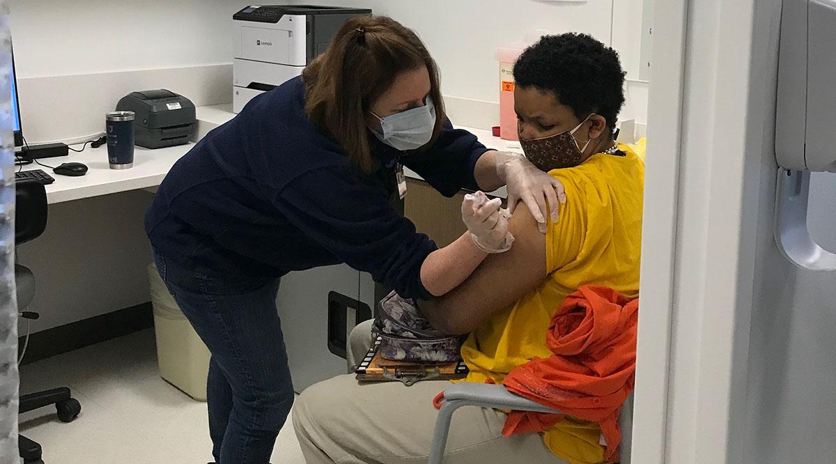 A nurse giving vaccine to a patient. Both are wearing face masks.