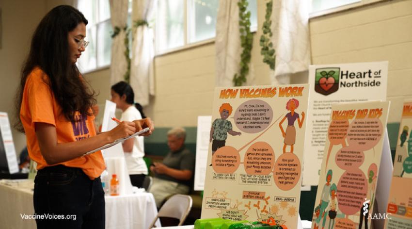 A health champion stands next to two posters that describe how vaccines work. 