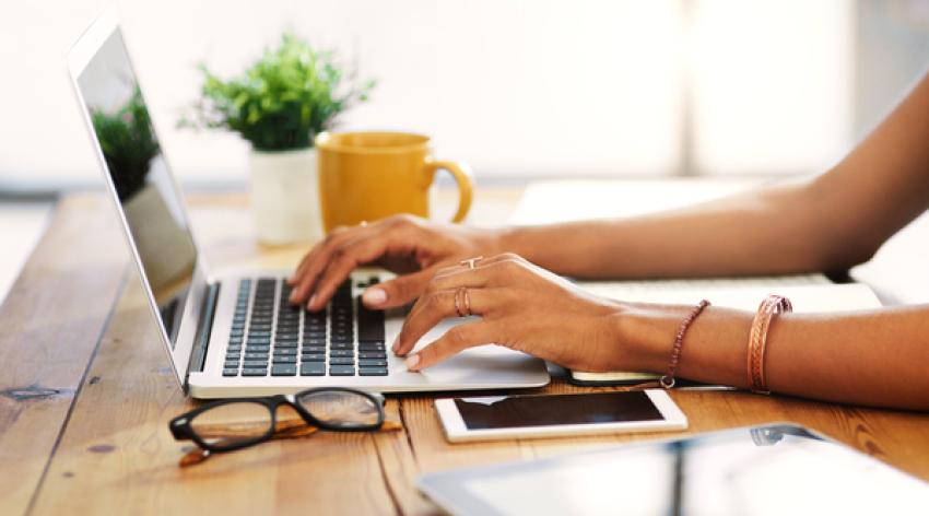 A person sitting at their desk and typing on their laptop.