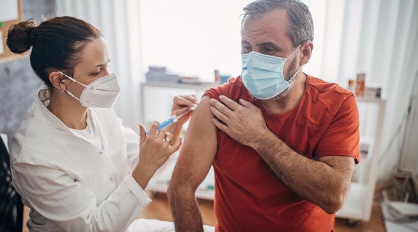 Young female doctor injecting vaccine in arm of senior man for immunization.