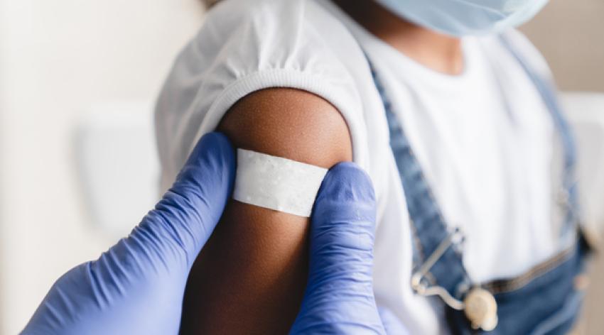 A gloved medical work places a band-aid on a masked child patient. 