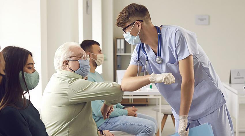 A male patient wearing face mask bumping elbows with a male doctor before getting vaccinated in a clinic.