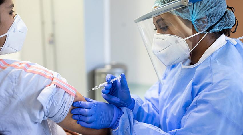 A doctor wearing masks and personal protective gear vaccinating a patient.